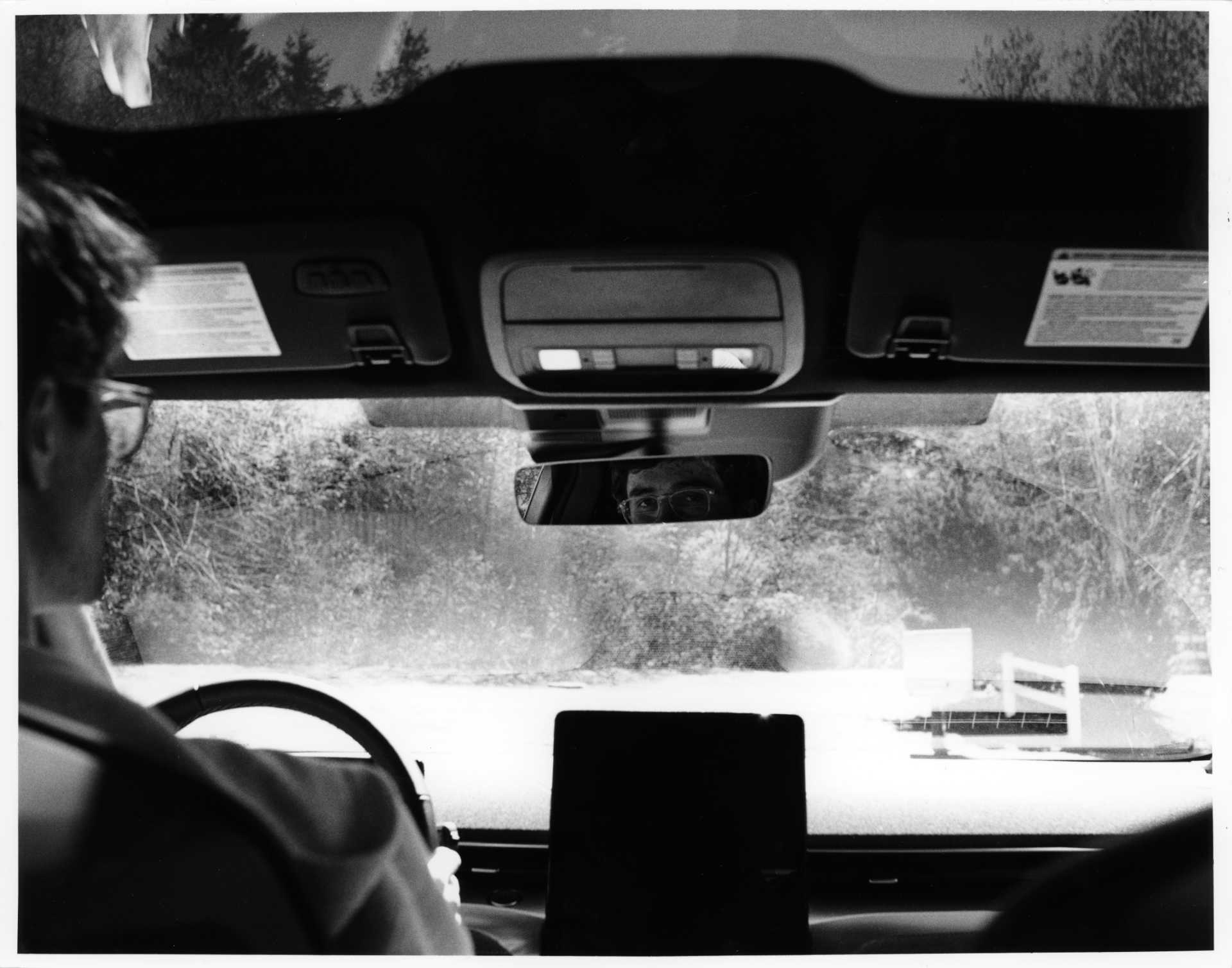 Black and white photo of me in the drivers seat of the car, looking back into the lens through the rearview mirror.