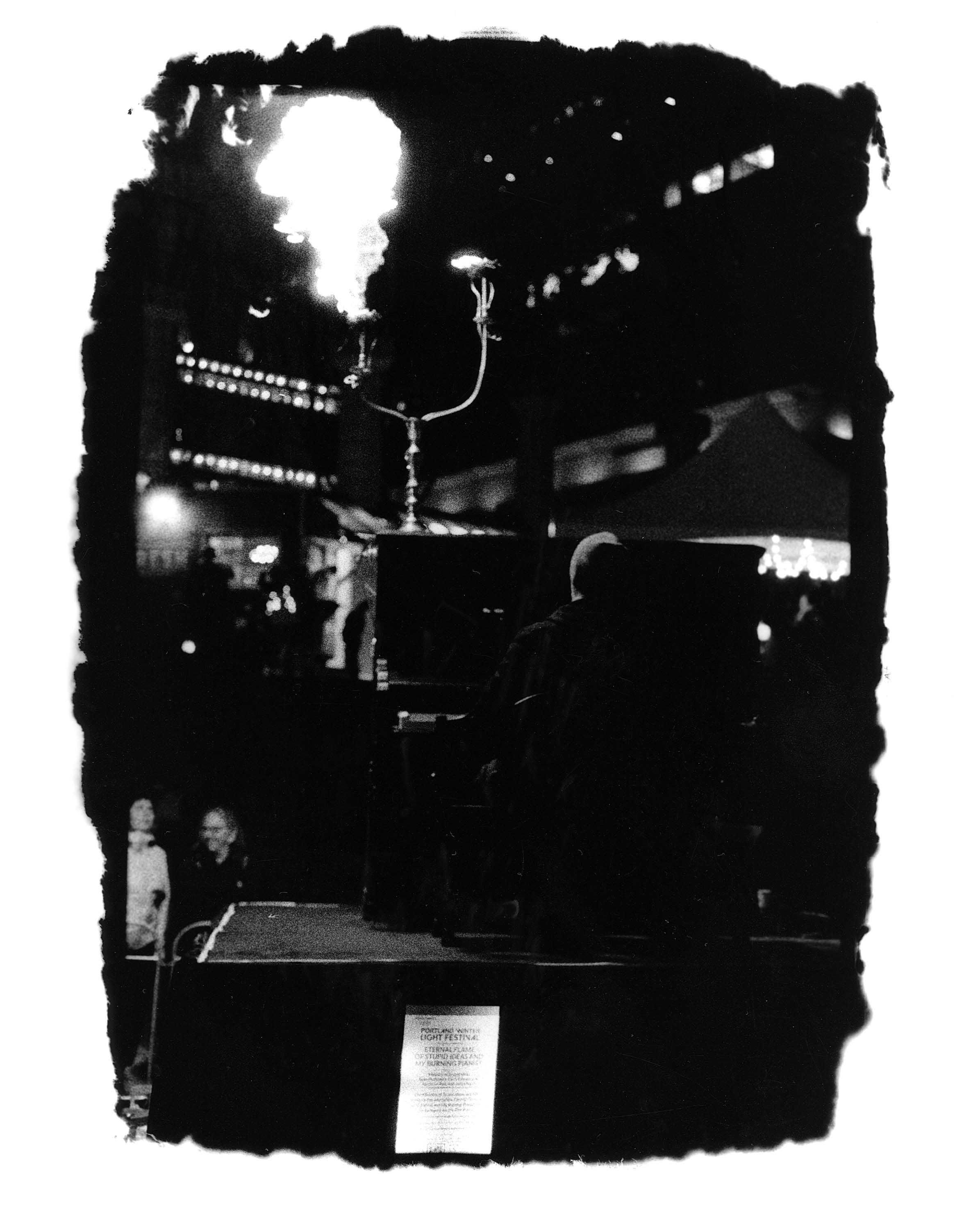 Black and white of a person playing piano with fire coming out of a candle holder on top.